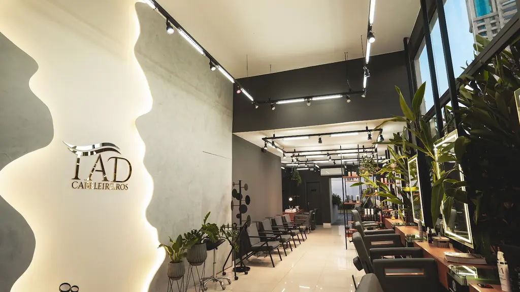 Corredor do TAD Cabeleireiros com a parede iluminada do logo, plantas e cadeiras de atendimento